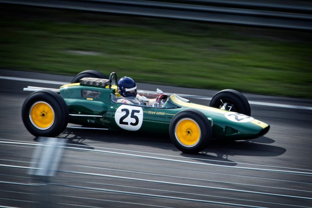 A green vintage Formula 1 car with number 25 speeds around a racetrack, showcasing classic racing heritage.